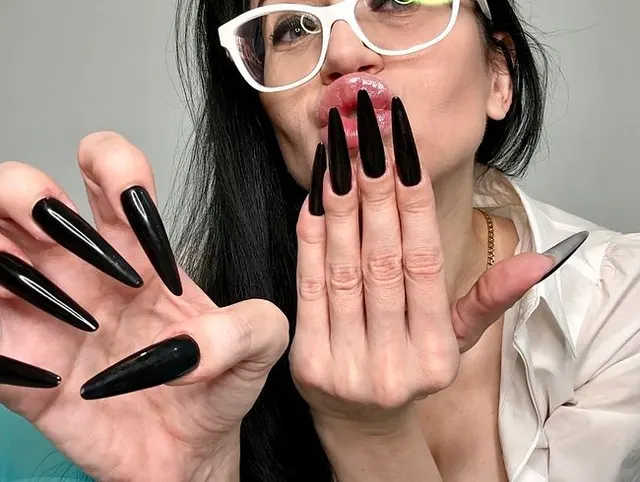 Lange schwarze Fingernägel und ein heißes Outfit mit Dessous, schwarzen Strümpfen, Bleistiftrock und weißer Bluse